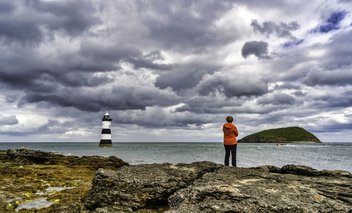 Rear view of man standing on rock by sea against sky