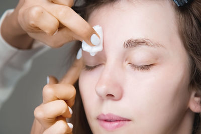 In a beauty salon, a master cosmetologist applies makeup and wipes eyebrows with a cotton pad. close