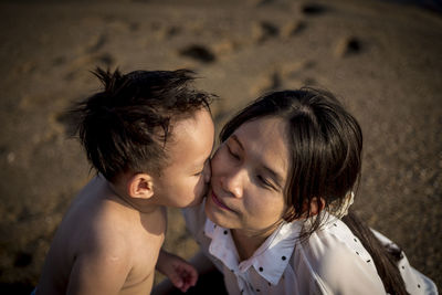 Shirtless son kissing mother at beach