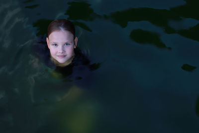 A 10-year-old girl swims in the evening in the dark water of the pool. portrait