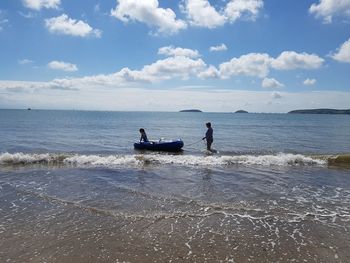 Grandmother and granddaughter with inflatable raft in sea against sky