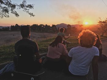 Rear view of people sitting on land against sunset sky