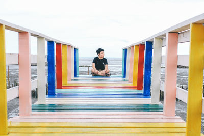 Full length of woman sitting on multi colored pier against sky