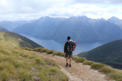 Rear view of man standing on dirt road against sky