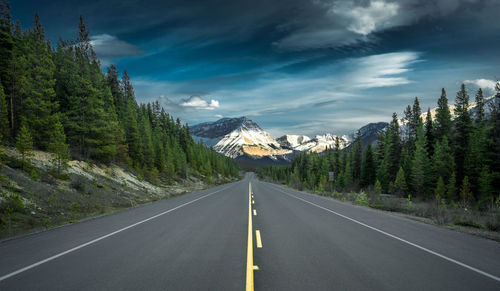 Empty road by trees against sky