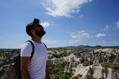 Young man standing on rock against sky