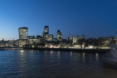 River by illuminated buildings against clear blue sky