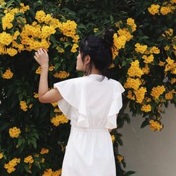 Rear view of woman standing by yellow flowering plants