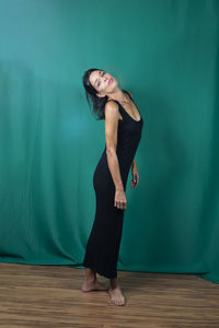 Portrait of standing adult model in black dress against dark green background. 