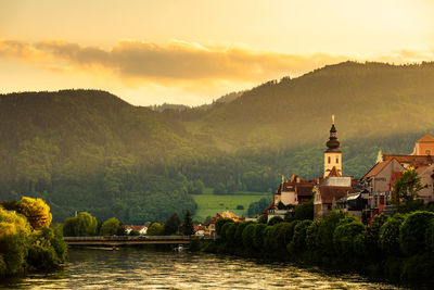 Buildings by river against sky during sunset