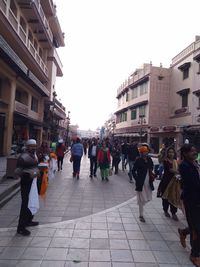 People walking on street amidst buildings in city against sky