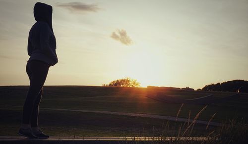 Side view of man standing on land against sky during sunset