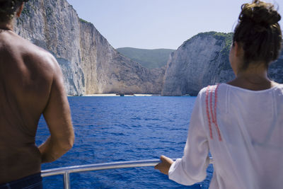 Rear view of man and woman standing on boat against sea