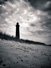 Lighthouse on landscape against cloudy sky