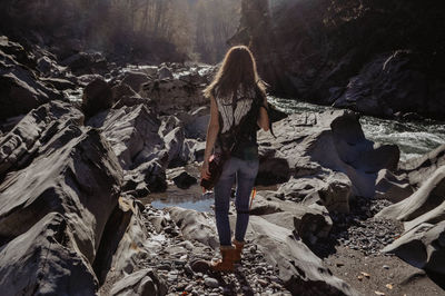 Rear view of woman walking on rocks in forest