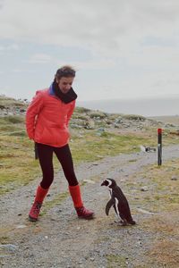 Woman and young penguin on field against sky