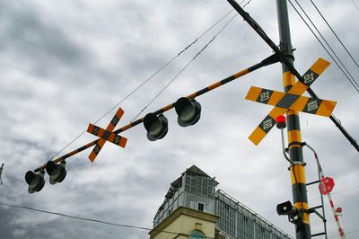 Low angle view of road signal by building against cloudy sky
