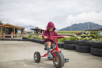 Young boy wearing hoody pedals oversized tricycle on racetrack.