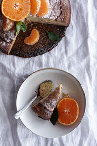 From above appetizing sweet cake and ripe orange mandarin cut and served on white plate on table