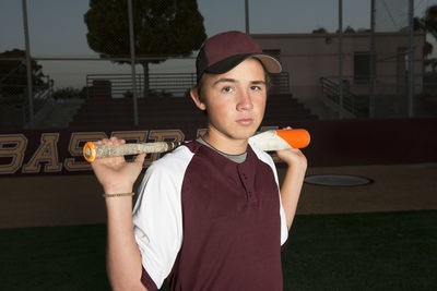 Portrait of a high school baseball player in maroon uniform holding his bat