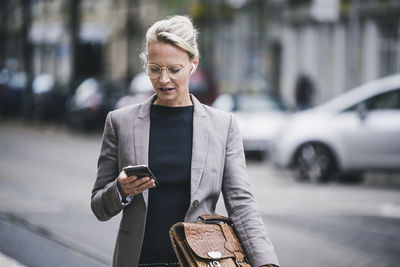 Blond female commuter holding bag while using smart phone