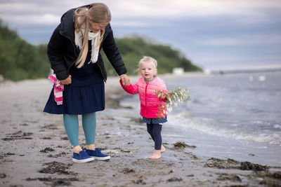 Pregnant woman standing with daughter at beach against sky