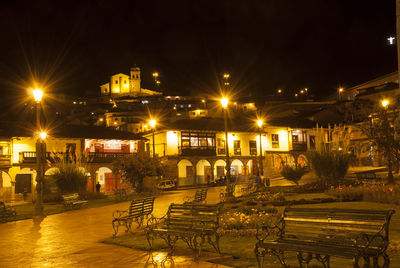 Illuminated street by buildings in city at night