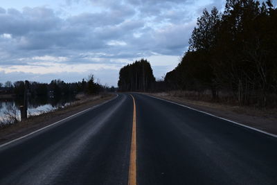 Empty road along trees and landscape against sky