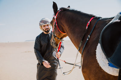 Man standing with horse on desert against sky