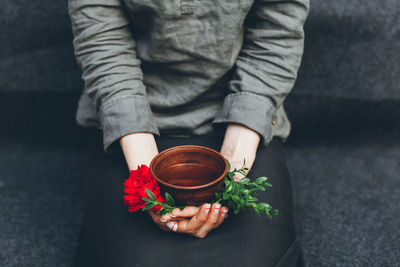 Midsection of woman holding flower and tea while sitting on sofa