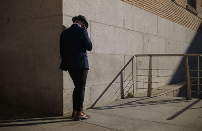 Full length of adult man in hat and suit taking on phone on street against wall. madrid, spain