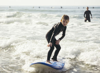 Full length of boy surfing in sea with father in background