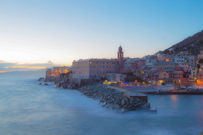 View of buildings by sea against clear sky in city during dusk