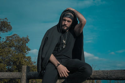 Young man looking away while sitting against sky