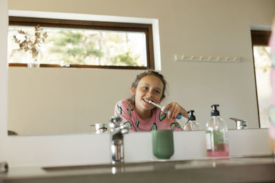 Girl brushing teeth reflecting in bathroom mirror