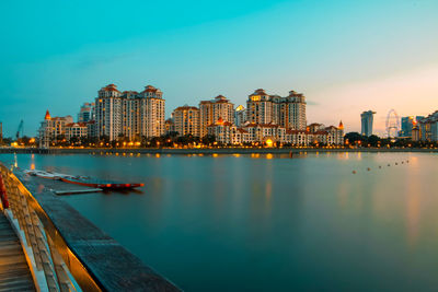 Illuminated buildings by river against sky in city