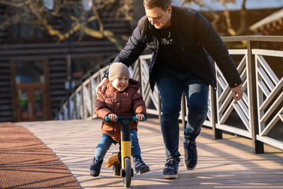 Happy father and son ride a bicycle on a bridge on a sunny day.