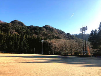 Road by trees and mountains against clear blue sky