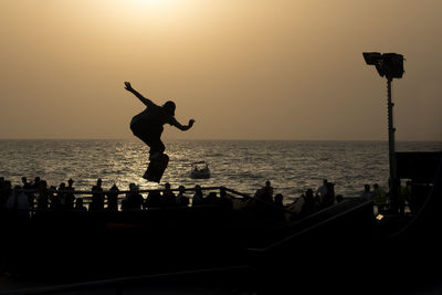 Silhouette people on sea against clear sky during sunset