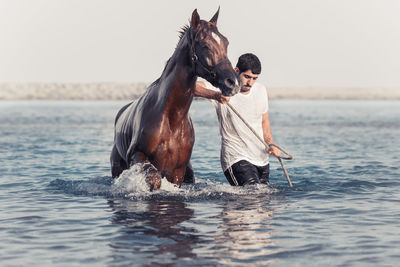 Man with horse in sea against sky