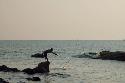 Fisherman throwing net on sea against sky