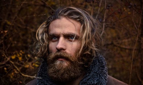 Close-up of thoughtful young man with beard against bare trees