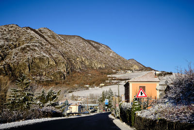 Road amidst buildings against clear blue sky