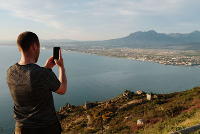 Rear view of man photographing with mobile phone against sea