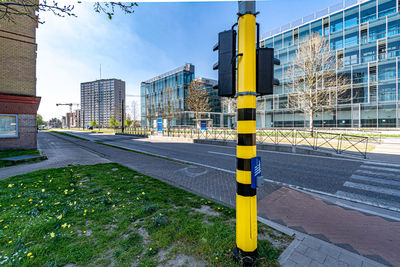 Yellow pole by road against buildings in city against sky