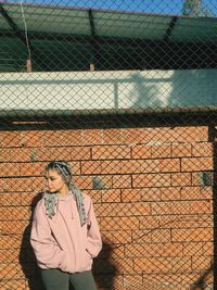 Full length of woman standing by chainlink fence