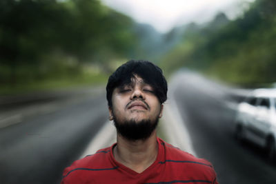 Young man with eyes closed standing by road