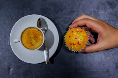 Cropped hand holding cupcake by tea over table