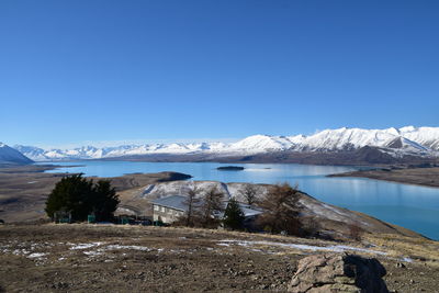 Scenic view of lake by snowcapped mountains against clear blue sky