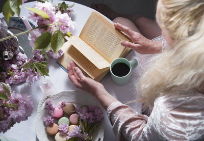 Blonde blogger in a pink dress drinks coffee, reads a book, uses a smartphone